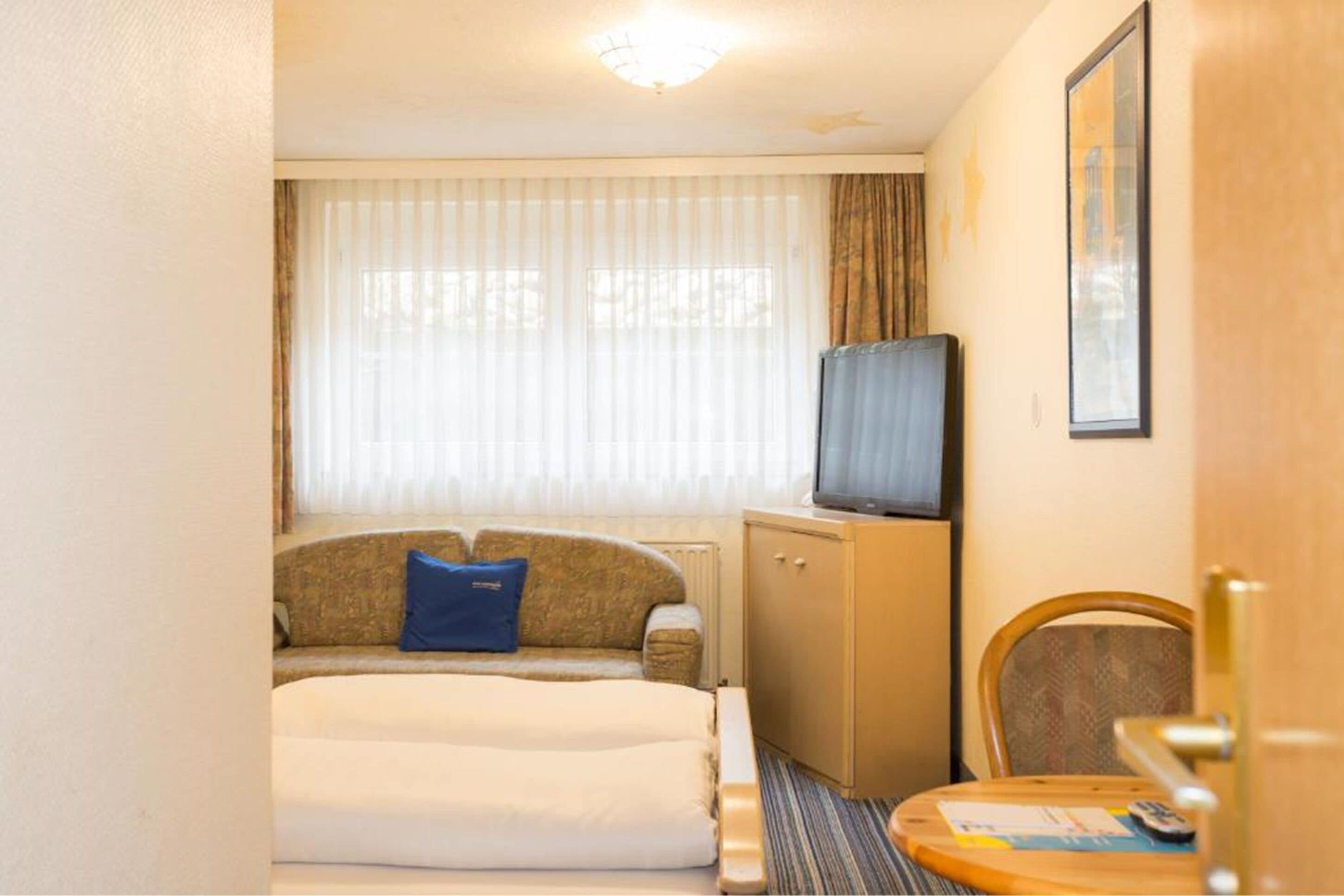 Une chambre d’hôtel avec un lit, un téléviseur posé sur un meuble, une chaise et une porte.