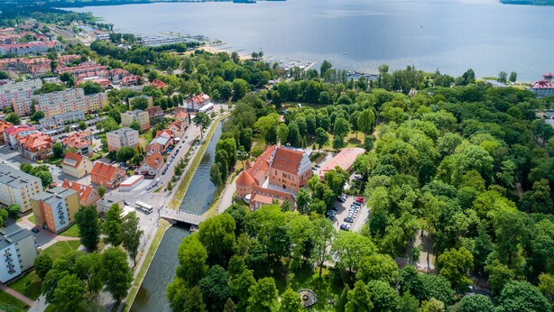Oversigtsbillede af en by med en flod, omgivet af grønt og bygninger.