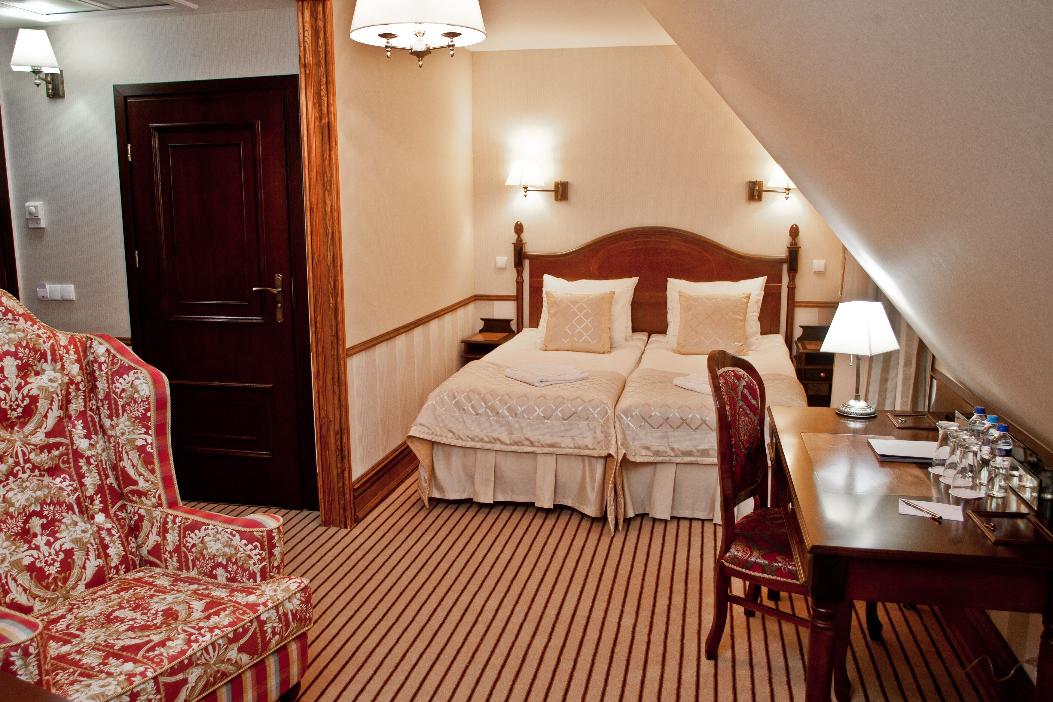 Una habitación de hotel con una cama doble, un escritorio con lámpara, una silla y una puerta.