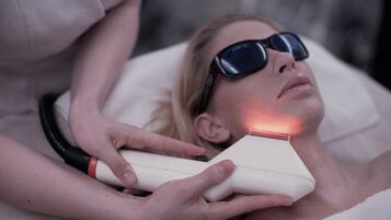 A person lying on a bed with a device emitting a red light near their head.