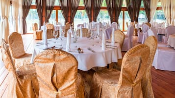 Un salón de banquetes con mesas redondas dispuestas para un evento formal, con manteles blancos y fundas doradas para las sillas.