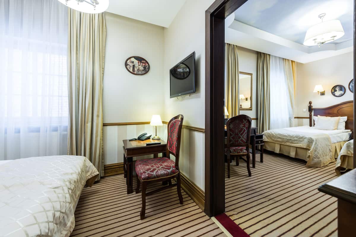 Habitación de hotel con dos camas, un escritorio con lámpara, una silla, un televisor y un espejo.