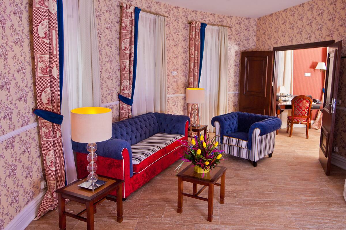 Una habitación con un sofá azul, cojines a rayas, una mesita con un jarrón de flores y un sillón a rayas.