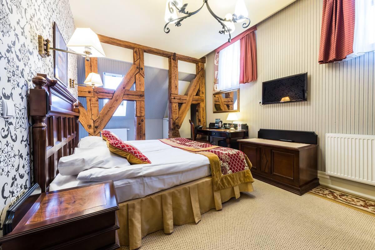 Un dormitorio tradicional con una cama con dosel, un escritorio de madera, un espejo y un radiador.