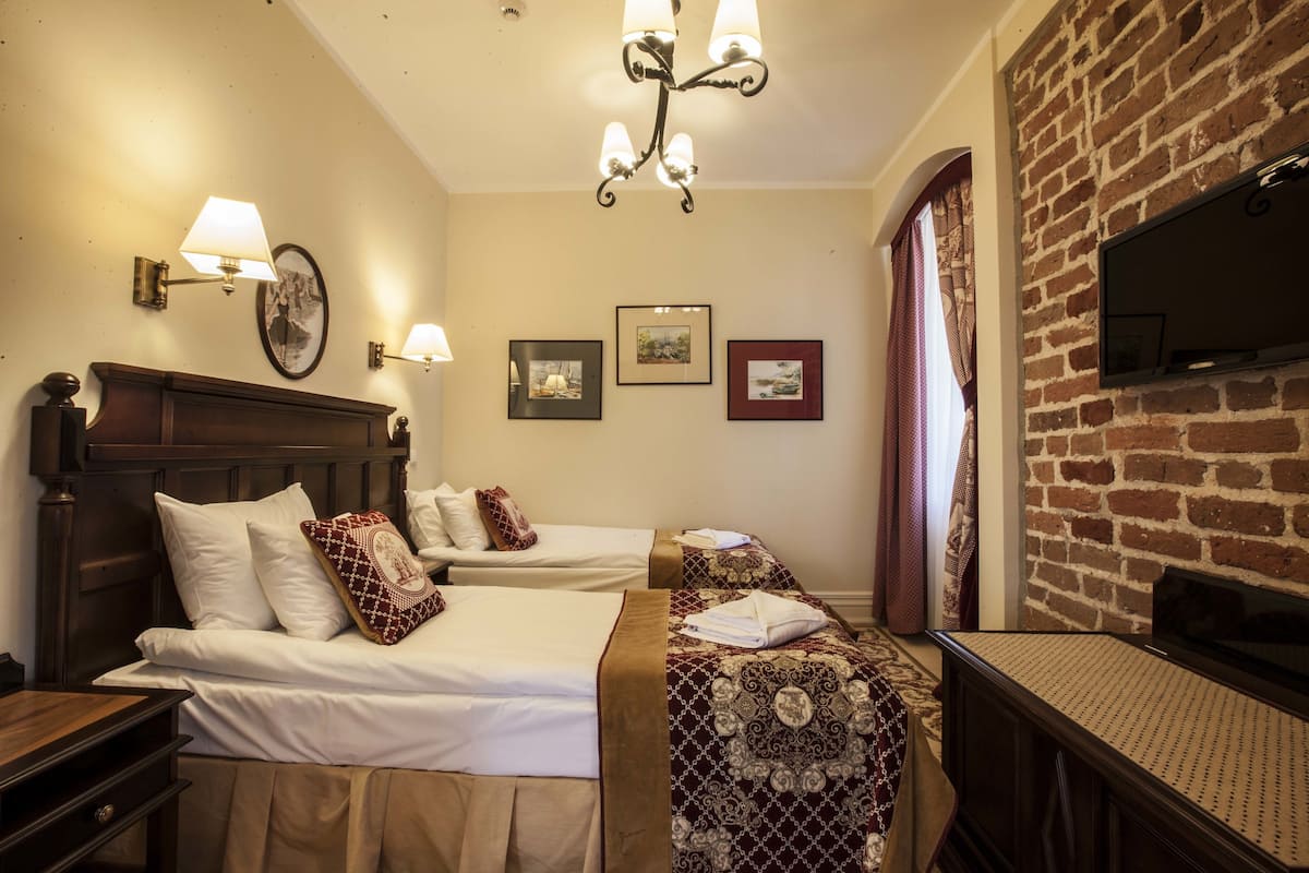Habitación de hotel con dos camas, un televisor instalado en una pared de ladrillo y un candelabro.