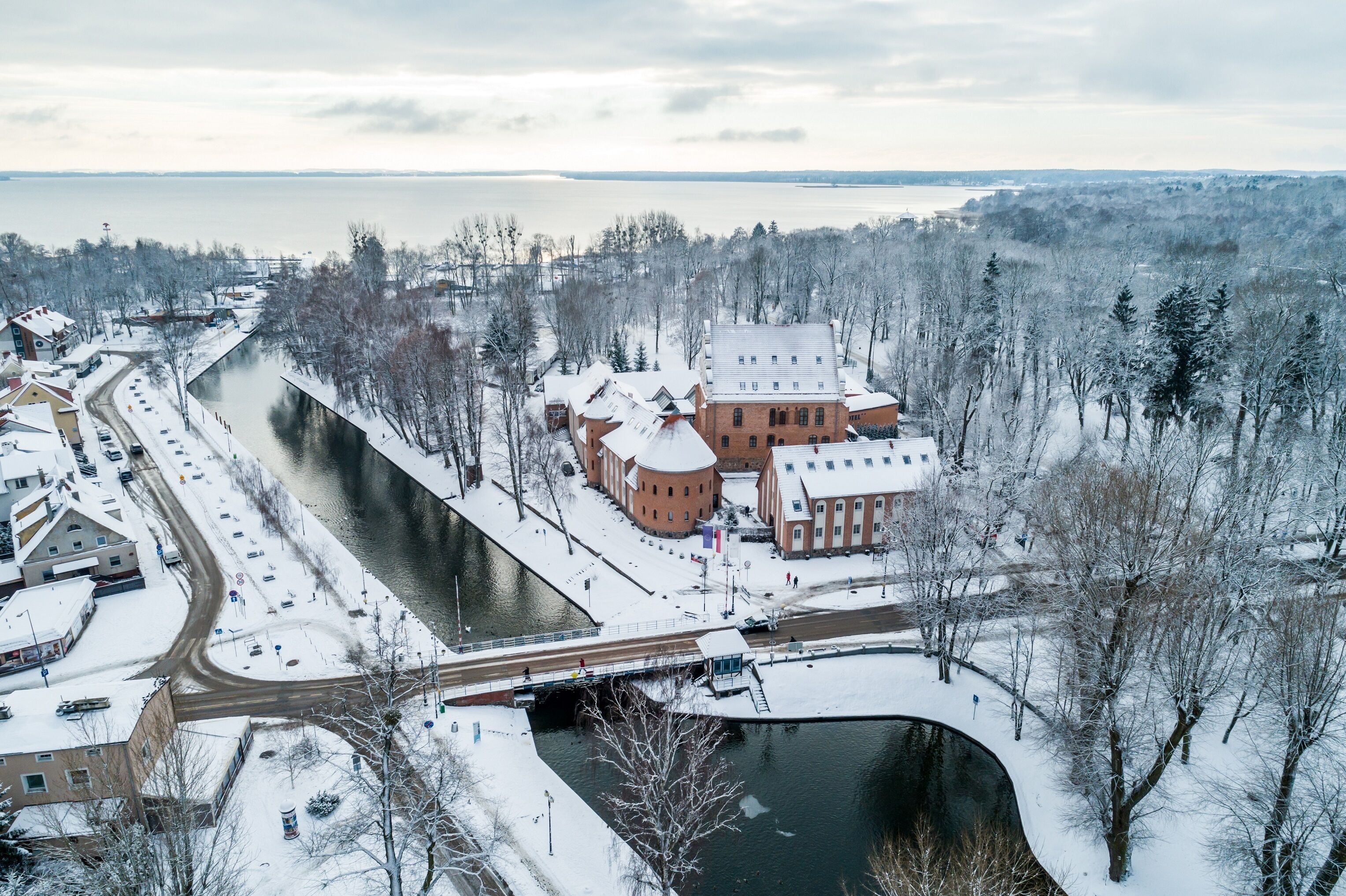Escena invernal con un río, edificios y árboles cubiertos de nieve.