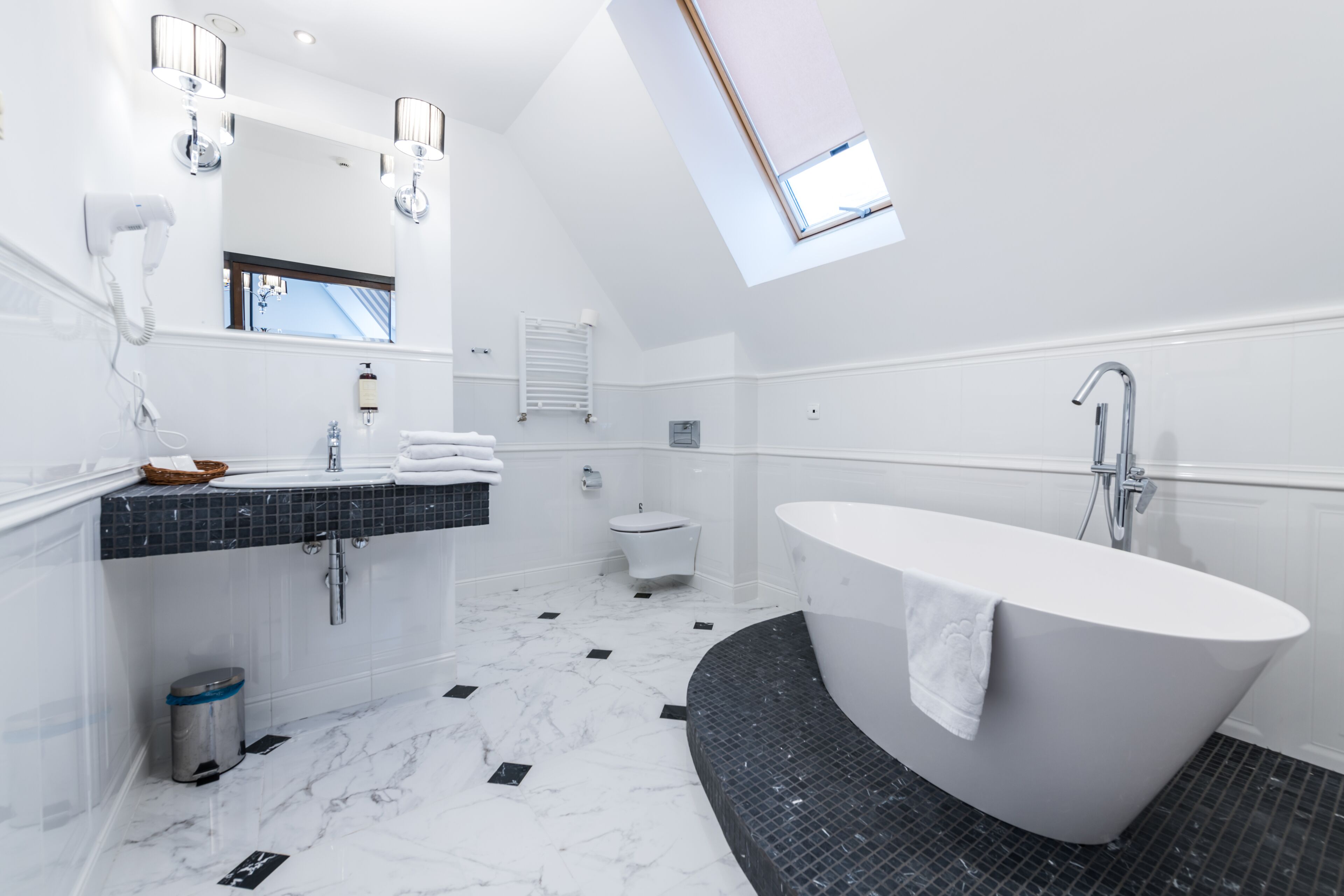 Een moderne badkamer met een vrijstaand bad, een grote spiegel en een dakraam.