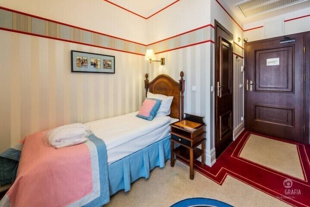 Una habitación de hotel con cama, mesita de noche, lámpara de pared y puerta.