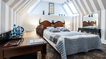 A bedroom with a sloped ceiling, a bed with a quilted cover, a wooden desk with a chair, and a mirror on the wall.