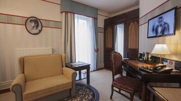 A hotel room with a sofa, a desk with a computer, a television, and a window with curtains.