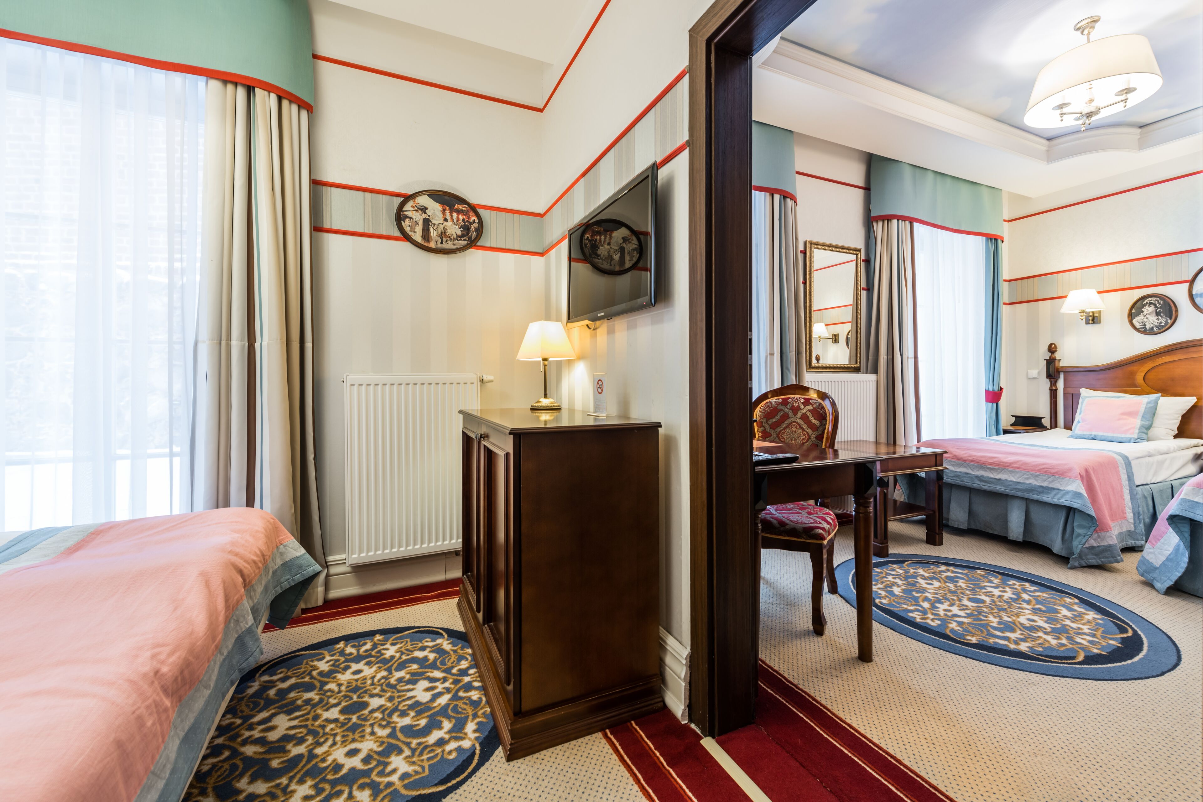 A hotel room with two beds, a desk, a chair, a dresser, and a large mirror.