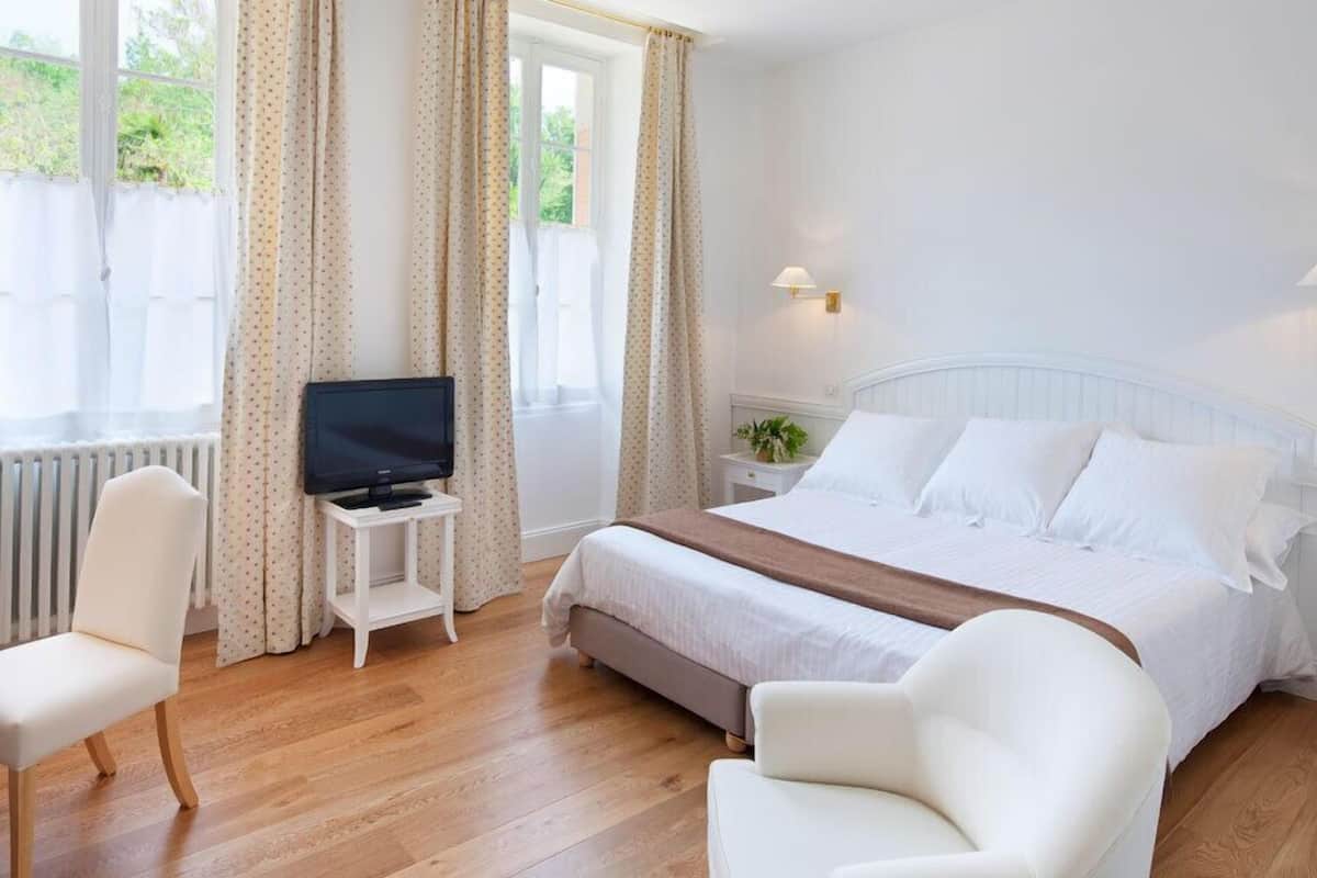 Ein Hotelzimmer mit einem Bett, einem Fernseher auf einem kleinen Tisch, einem Sessel und einem Nachttisch mit einer Lampe.