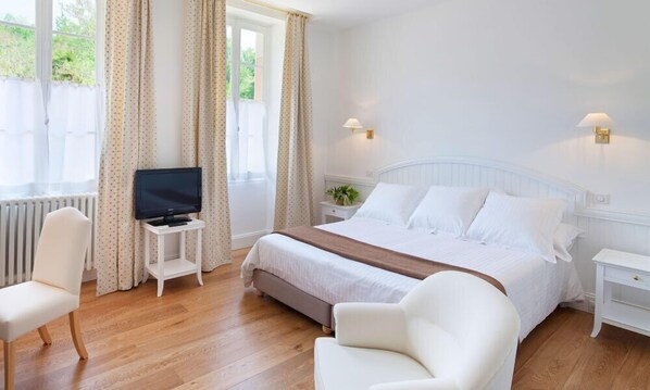 A hotel room with a bed, a television on a small table, a chair, and a bedside table with a lamp.