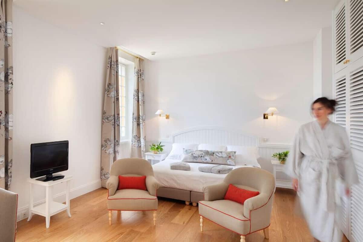 Ein Hotelzimmer mit einem Bett, zwei Sesseln, einem Fernseher und einem Kleiderschrank.