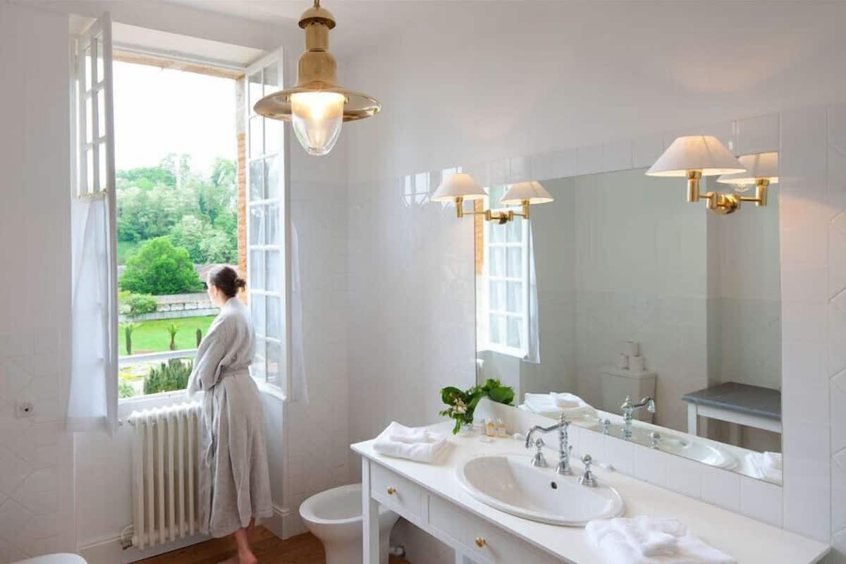 Ein Badezimmer mit großem Fenster, weißem Waschbecken, Spiegel und Heizkörper.