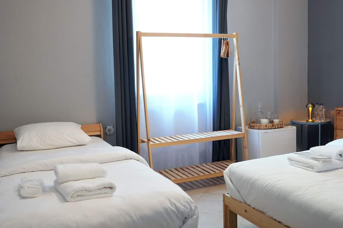 A hotel room with two beds, a wooden ladder, a small table with a lamp, and a window with curtains.