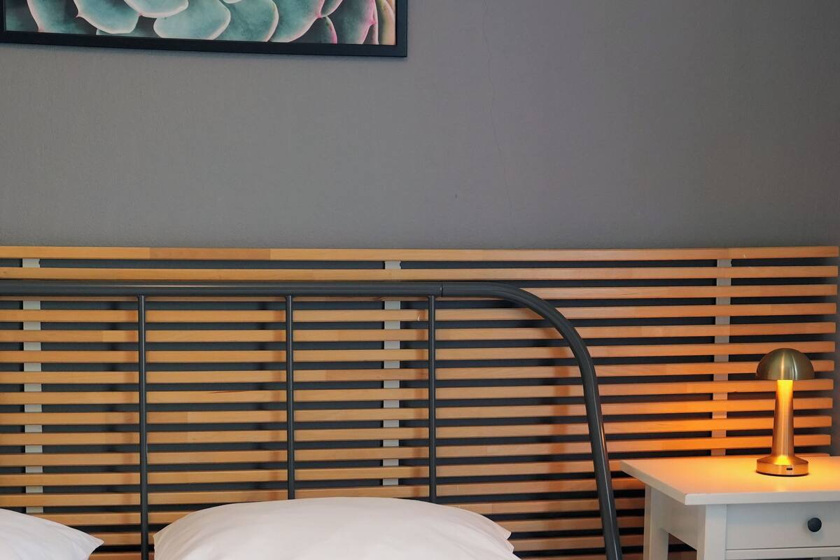 A bed with white bedding, a wooden slatted headboard, and a bedside table with a lamp.