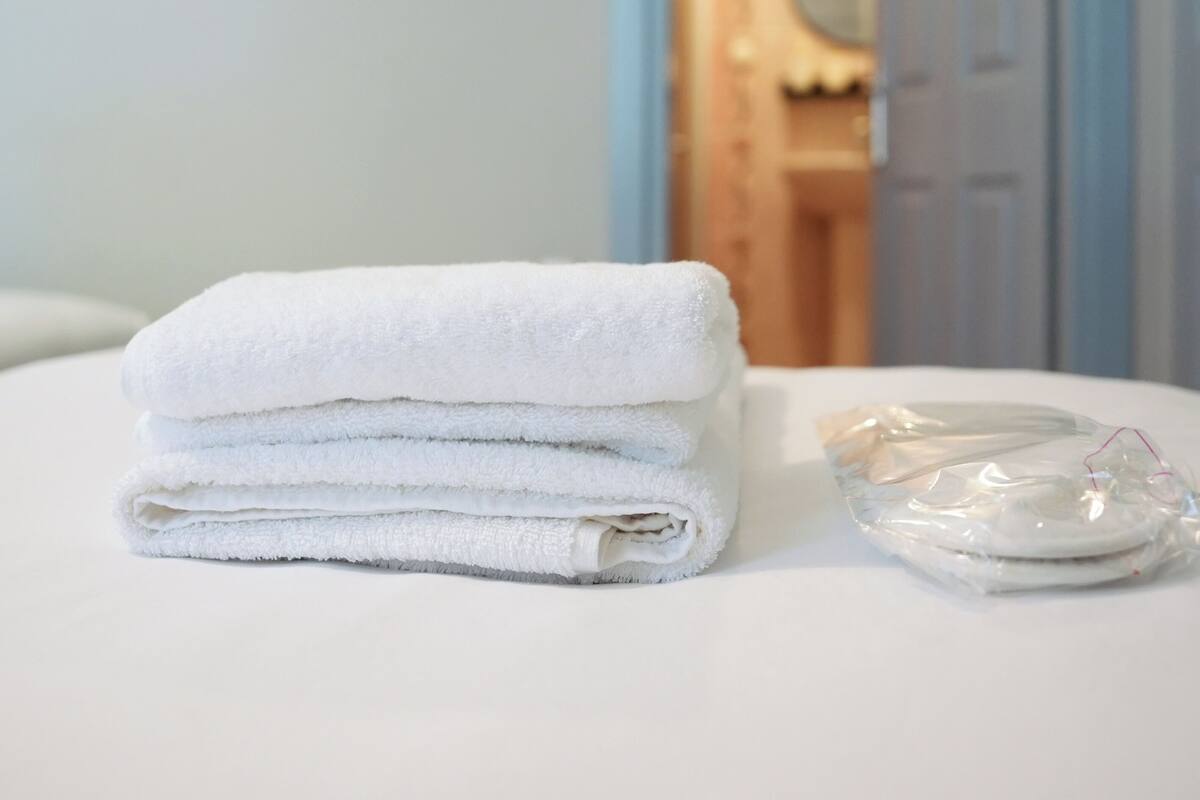 A stack of white towels on a white table in a room with a wooden door and a mirror in the background.