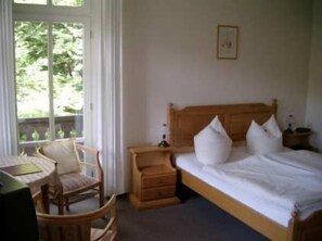 A bedroom with a wooden bed, white pillows, a wooden nightstand, a wooden chair, and a window with curtains. - Bilz Pension (Moritzburg)