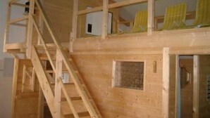 Una cabaña de madera con habitación en el altillo, escalera y ventana con cortinas amarillas.