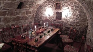 Un comedor con paredes de piedra y una larga mesa de madera dispuesta para una comida, rodeada de sillas de madera.
