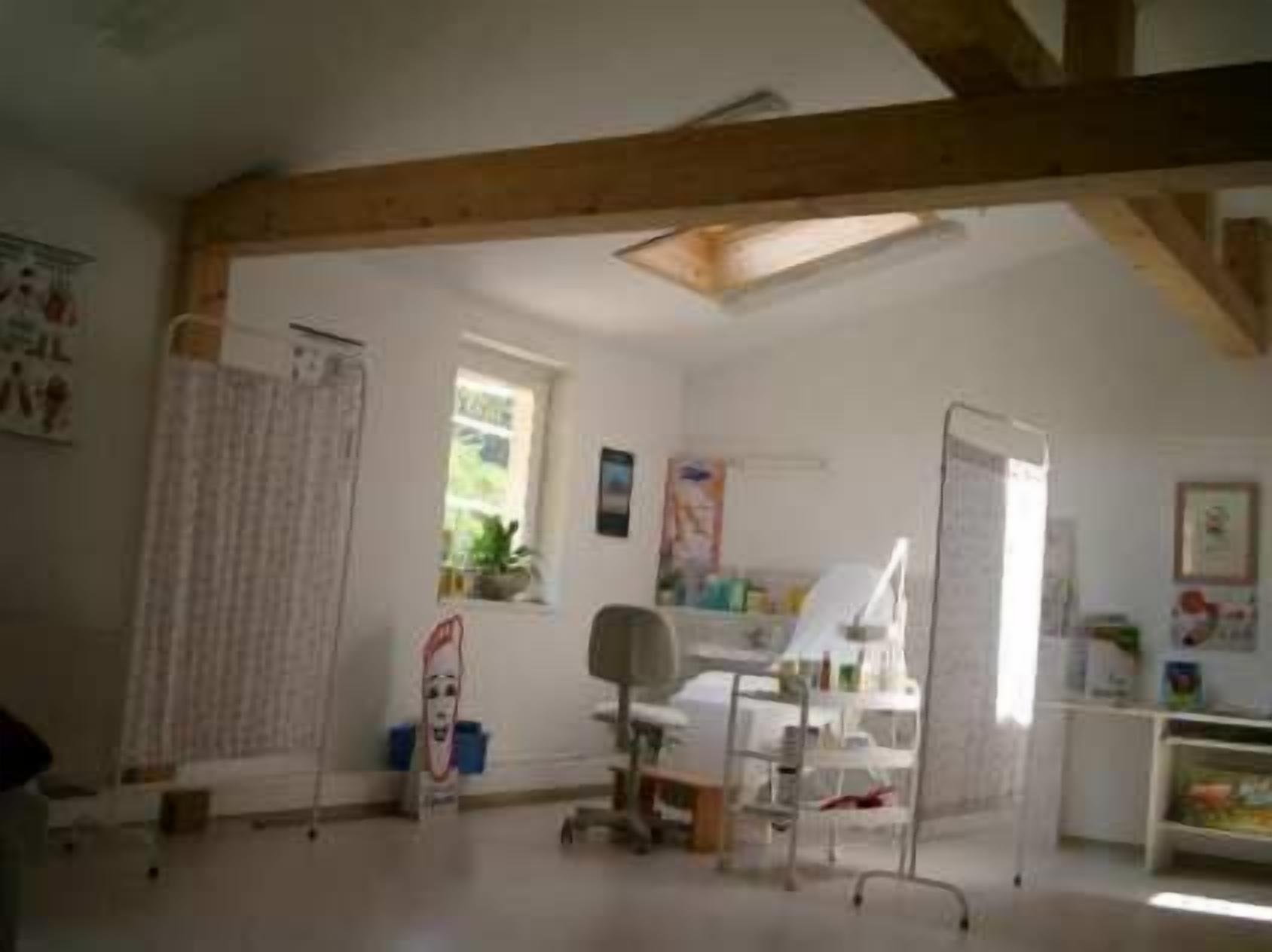 Ein Zimmer mit schrägem Dach, einem Schreibtisch mit Stuhl, einem Fenster und diversen Gegenständen auf Regalen.
