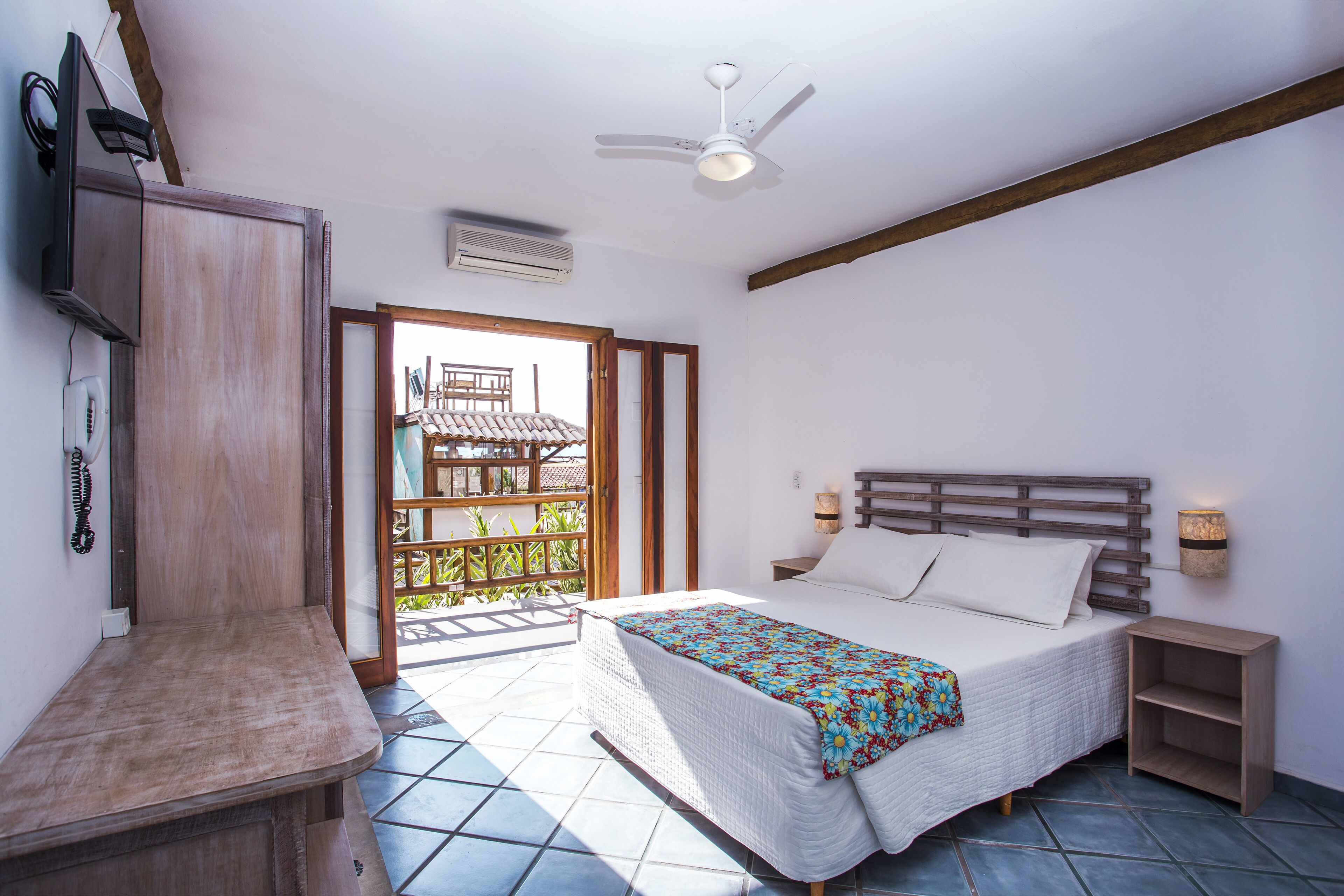 A bedroom with a bed, bedside tables, a ceiling fan, and a view of a balcony.