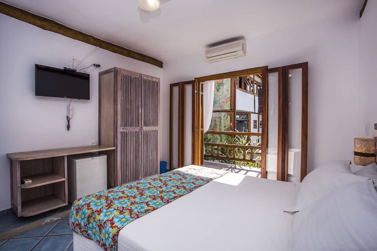 A bedroom with a bed, a TV mounted on the wall, a desk, and a small refrigerator.