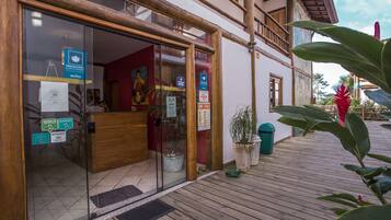 Uma área de recepção com uma mesa de madeira, portas de vidro e diversos avisos, incluindo a obrigatoriedade de uso de máscara.