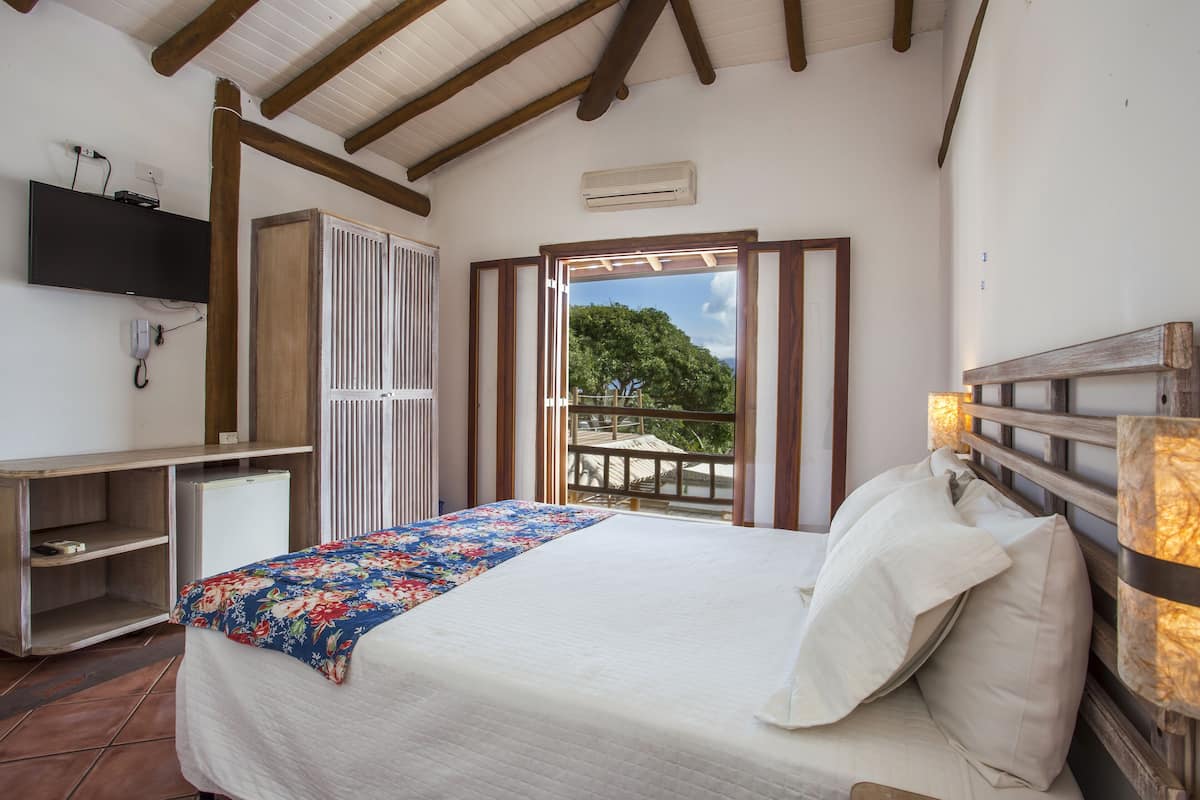 A bedroom with a bed, a desk, a TV, and a window with a view of trees.