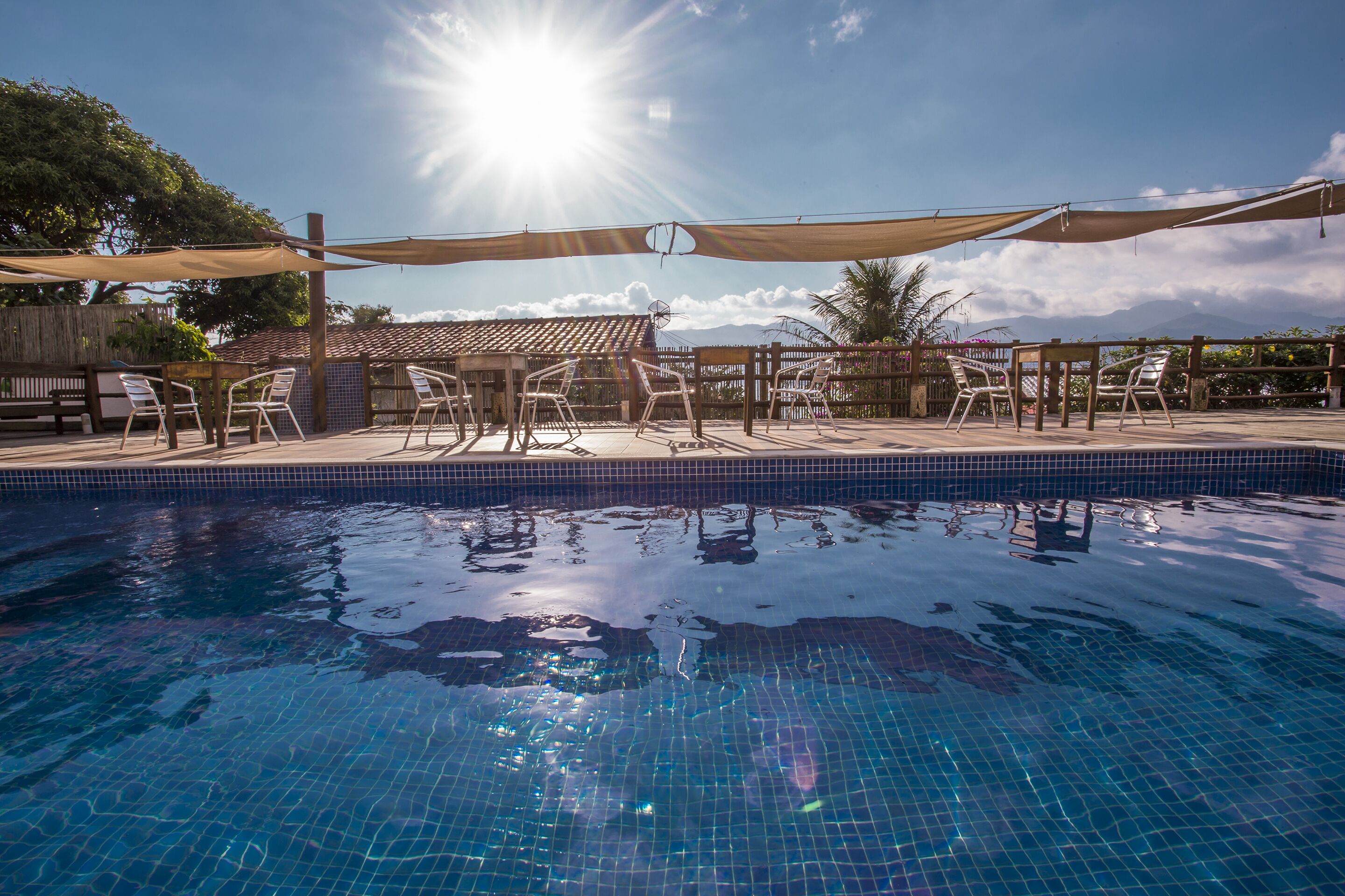 Uma piscina com água azul cristalina, rodeada por um deck de madeira e cadeiras brancas.