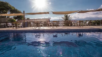 Uma piscina com água azul cristalina, rodeada por um deck de madeira e cadeiras brancas.