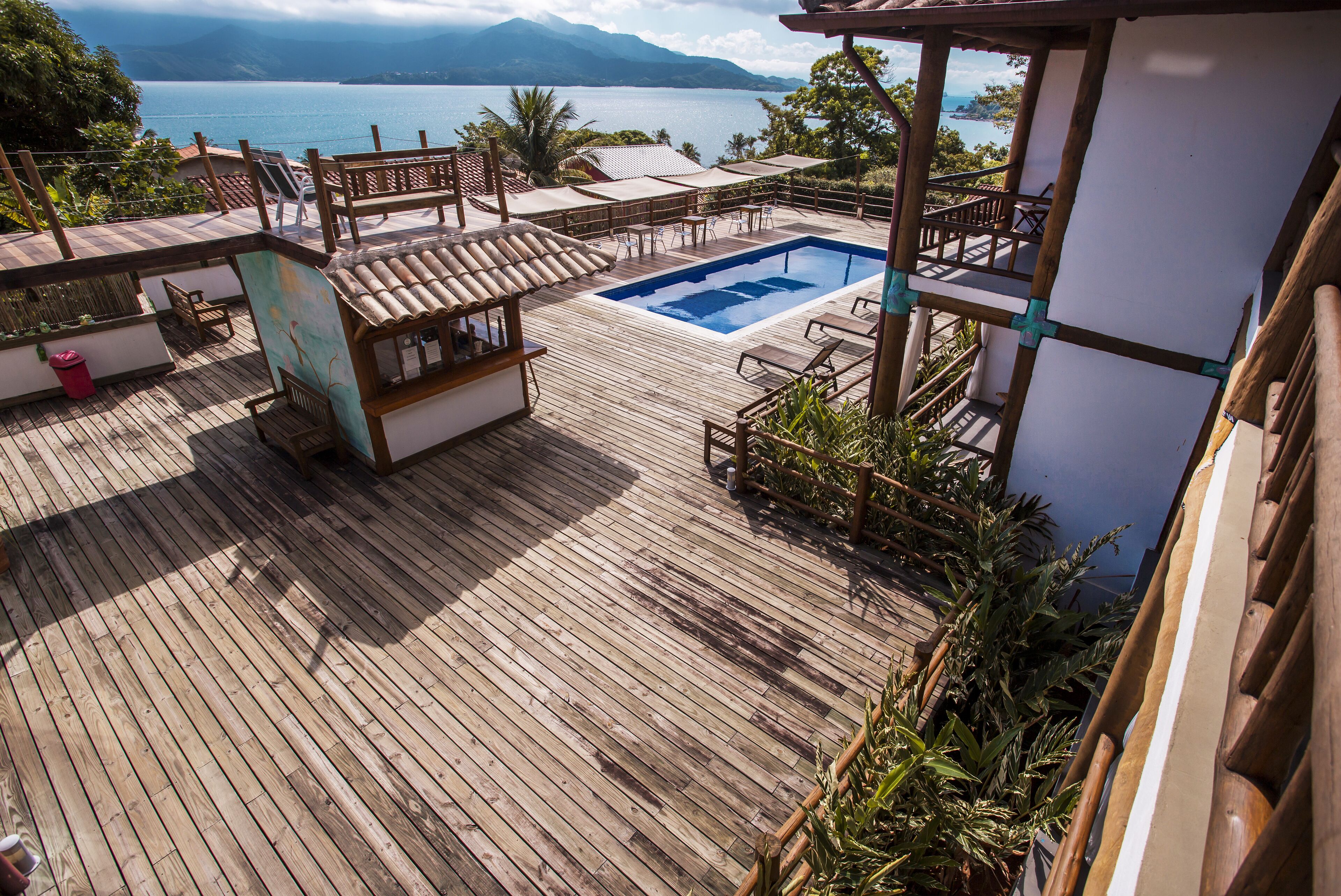Um deck de madeira com piscina, móveis de exterior e vista para o mar.