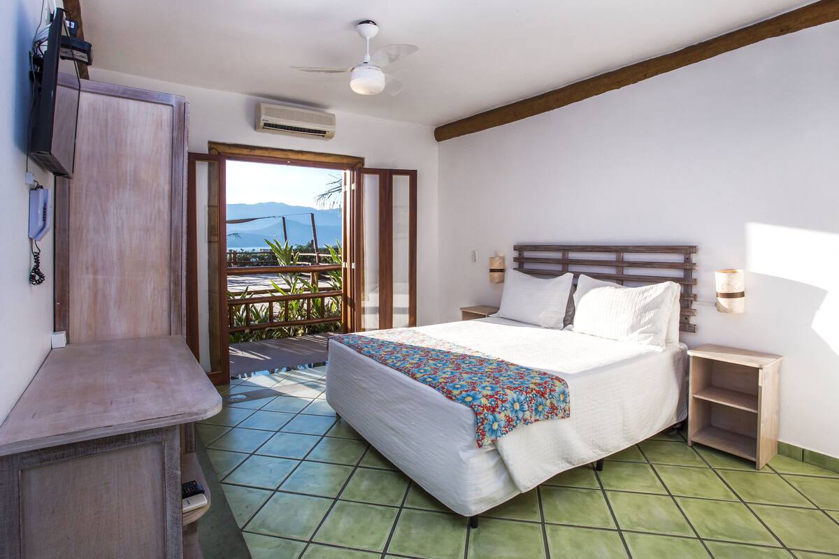 A bedroom with a bed, bedside tables, a ceiling fan, and a view of the outdoors.