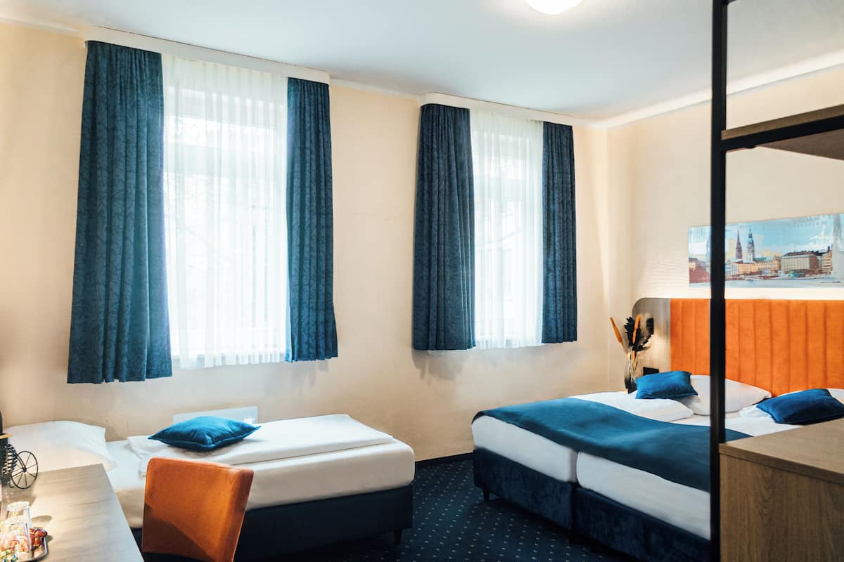 Hotellihuone, jossa on kaksi sänkyä, työpöytä ja tuoli.