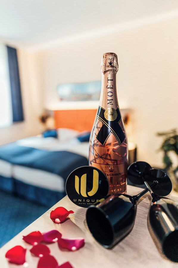 Una botella de champán, un par de gafas y pétalos de rosa sobre una mesa en una habitación de hotel.