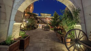 An arched entrance to a building with a stone pathway leading to a seating area with potted plants and a wooden bench. - Roma Cave Suite Hotel (Nevsehir)