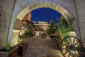 An arched entrance to a building with a stone pathway leading to a seating area with potted plants and a wooden bench. - Roma Cave Suite Hotel (Nevsehir)