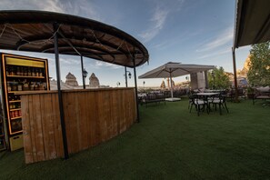 An outdoor seating area with a wooden bar and umbrellas, overlooking a scenic landscape.