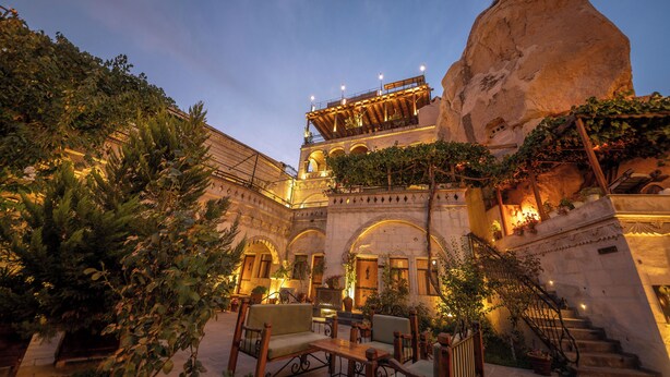 A courtyard with stone architecture, outdoor seating, and a large rock formation. - Roma Cave Suite Hotel (Nevsehir)