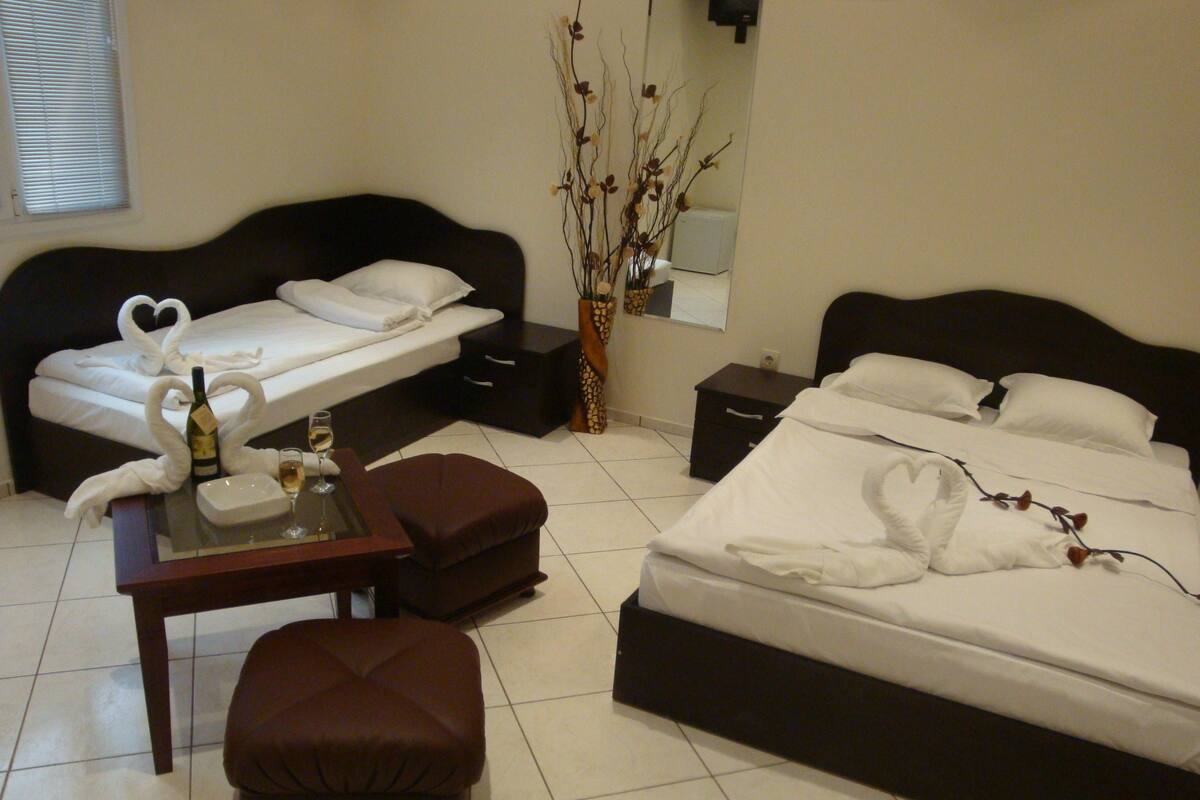 A hotel room with a bed, a small table with a bottle and glass, a chair, and a nightstand.
