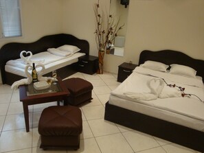 A hotel room with a bed, a small table with a bottle and glass, a chair, and a nightstand. - Hotel Niagara (Varna)