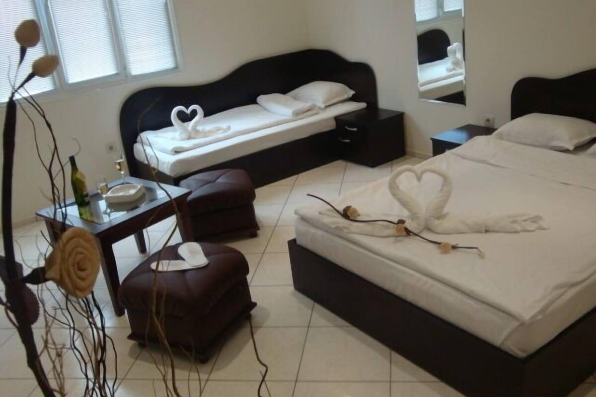 A bedroom with a bed, a bedside table, a nightstand, a dresser, and a window with blinds.