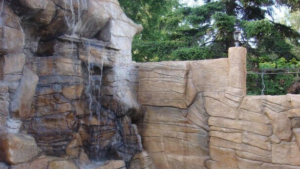 Piscina com cascata rochosa, parede de pedra e um poste de luz.