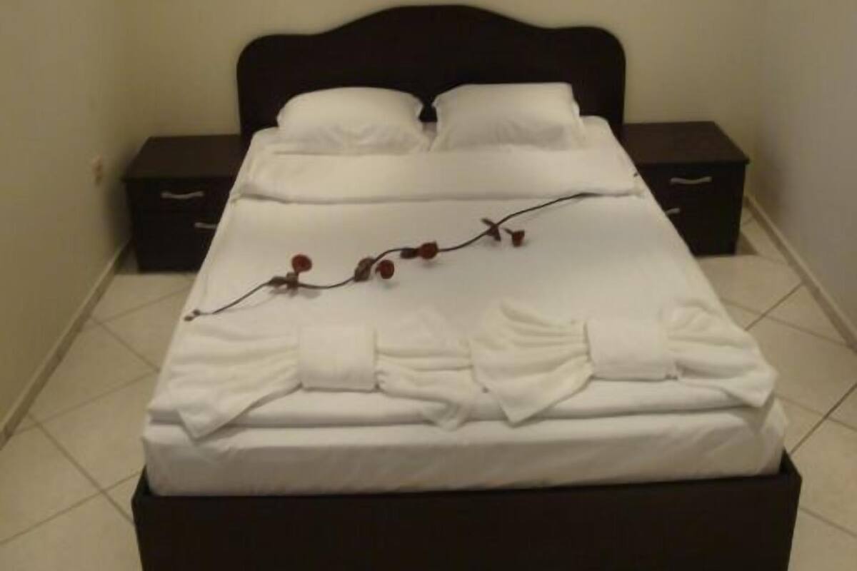 A neatly made bed with white linens and a decorative branch, a dark headboard, and a wall-mounted air conditioner.