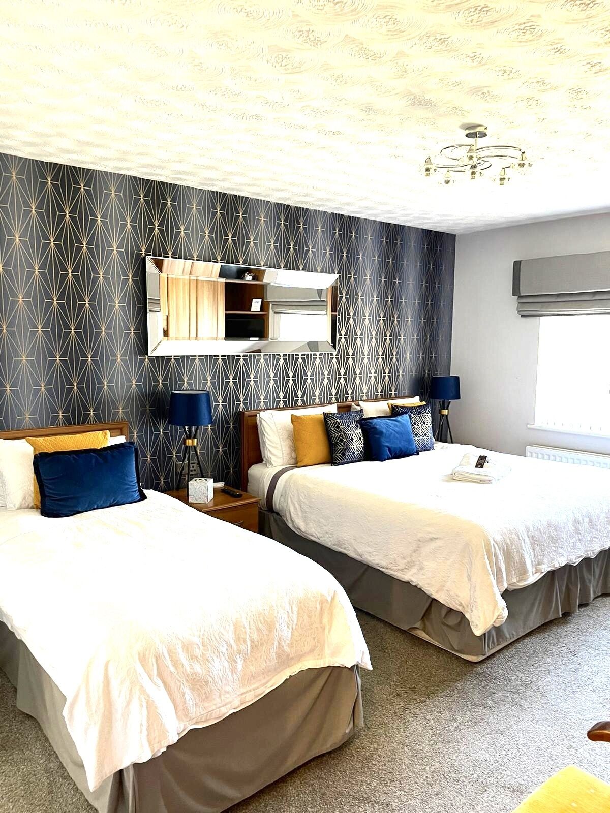 Habitación de hotel con dos camas, un espejo grande y un aplique de techo.