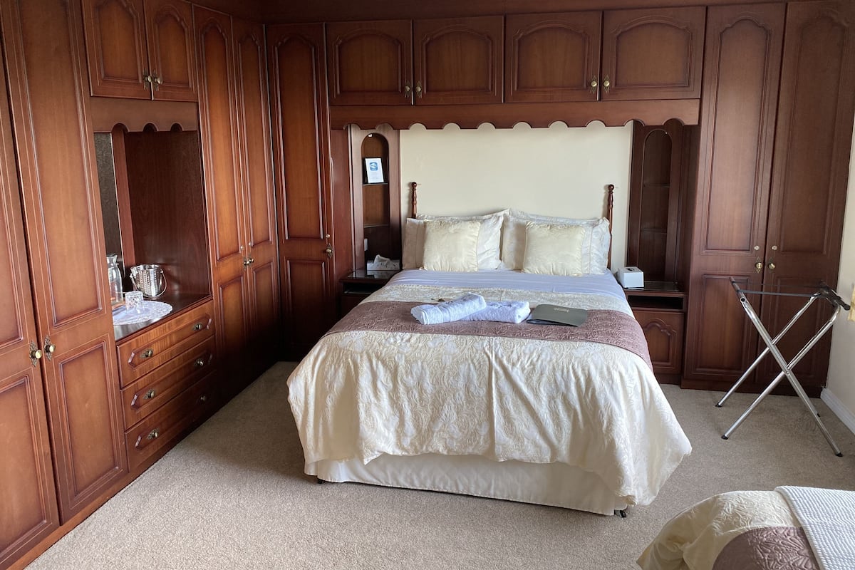 A bedroom with a large bed, wooden wardrobe, and a small table.