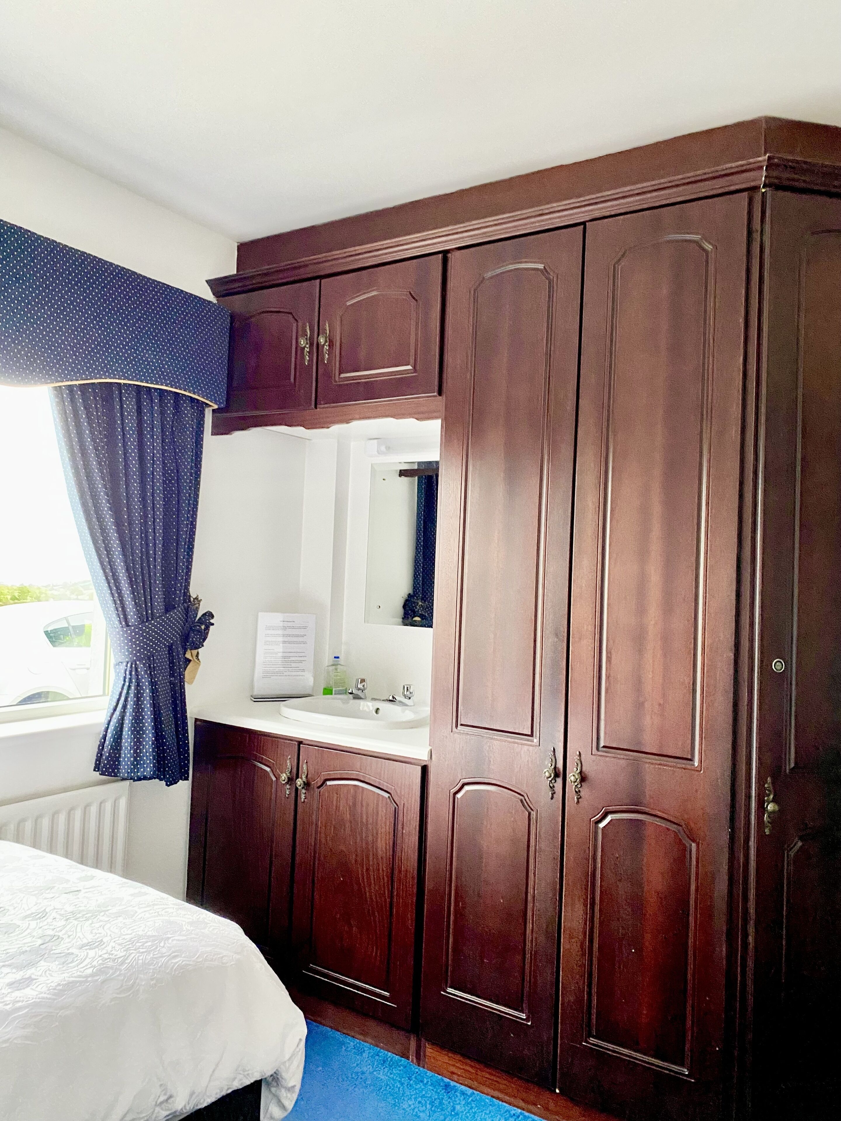 Une chambre à coucher avec un lit, une commode, un miroir et une fenêtre avec des rideaux.