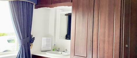 A bedroom with a bed, a dresser, a mirror, and a window with curtains.