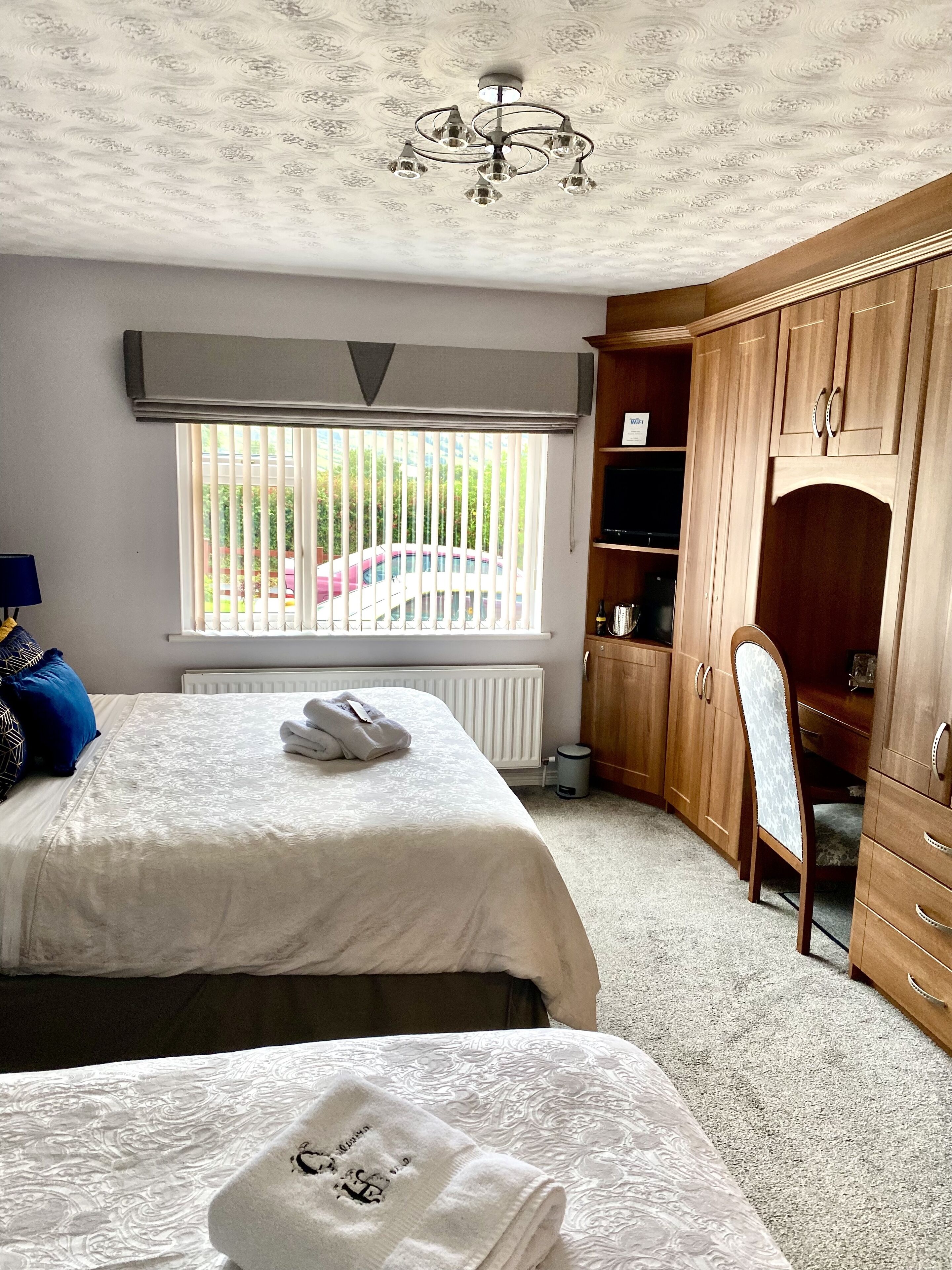 Ein Schlafzimmer mit zwei Betten, einem Holzschrank, einem Heizkörper und einem Fenster mit Jalousien.